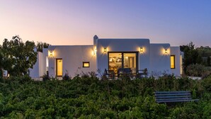 A modern building with a dining area, a bench, and a well-lit entrance. - Country House 'A The' with Mountain View, Shared Terrace and Wi-Fi (Tinos)