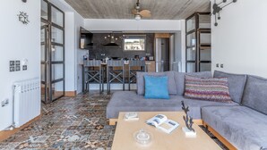 A modern living room with a grey sofa, a coffee table, and a view into the kitchen. - Country House 'A The' with Mountain View, Shared Terrace and Wi-Fi (Tinos)