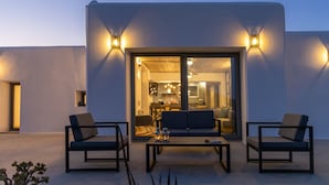 A modern outdoor seating area with two chairs and a table, a glass door leading to an interior space, and wall-mounted lights. - Country House 'A The' with Mountain View, Shared Terrace and Wi-Fi (Tinos)