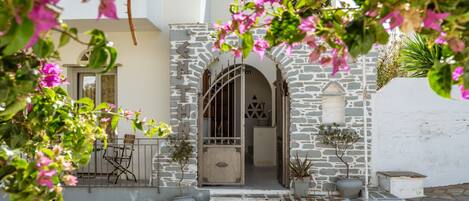 A stone building with a white facade, a wooden door, and a small balcony with chairs.