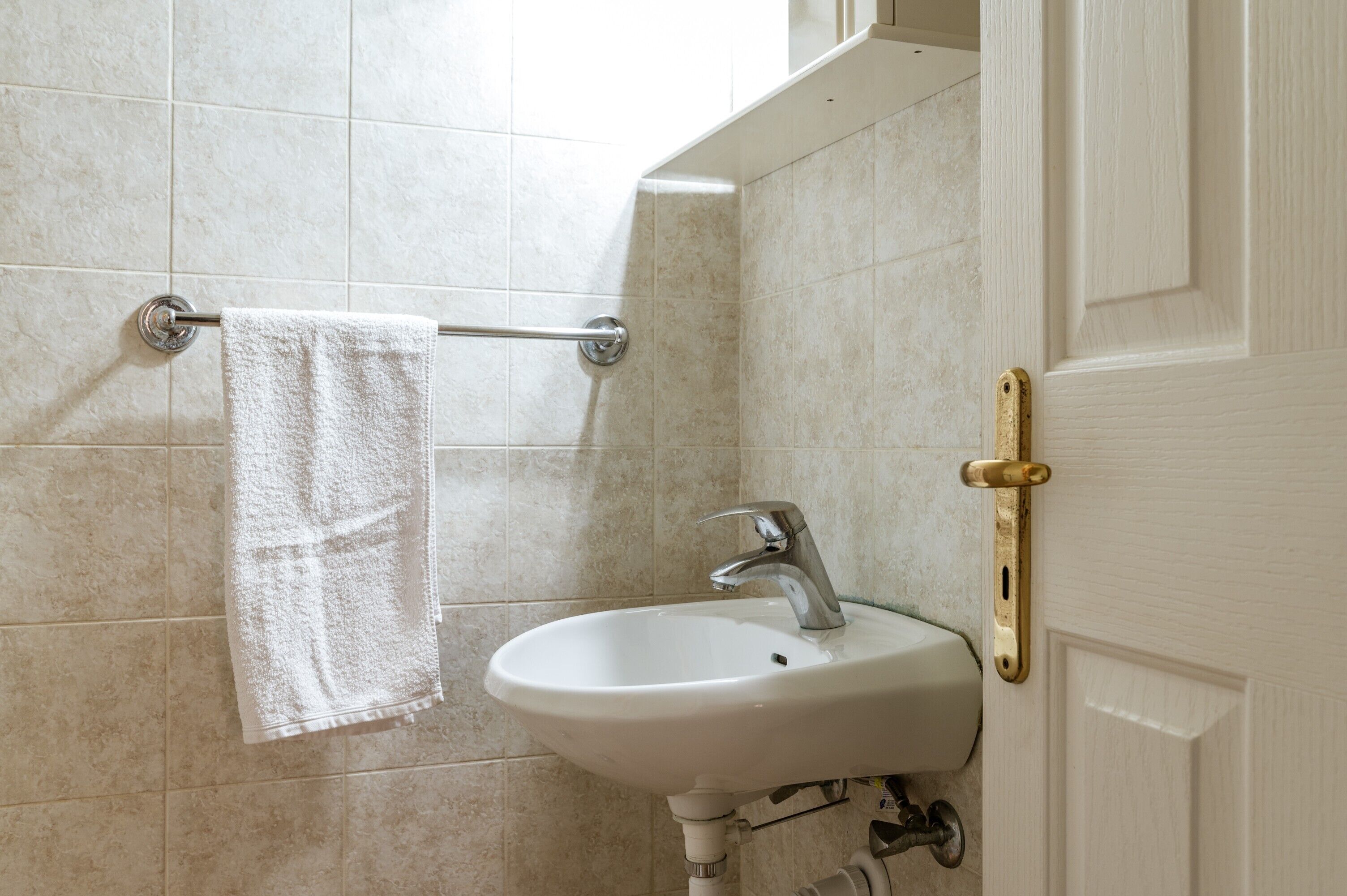Une salle de bain avec un lavabo blanc, une serviette suspendue à un porte-serviettes et une porte dotée d’une poignée en laiton.