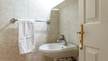 Une salle de bain avec un lavabo blanc, une serviette suspendue à un porte-serviettes et une porte dotée d’une poignée en laiton.