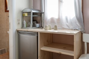 Una cucina compatta con lavastoviglie integrata, un piccolo frigorifero, un mobiletto metallico con oggetti da cucina e una finestra con tende leggere.