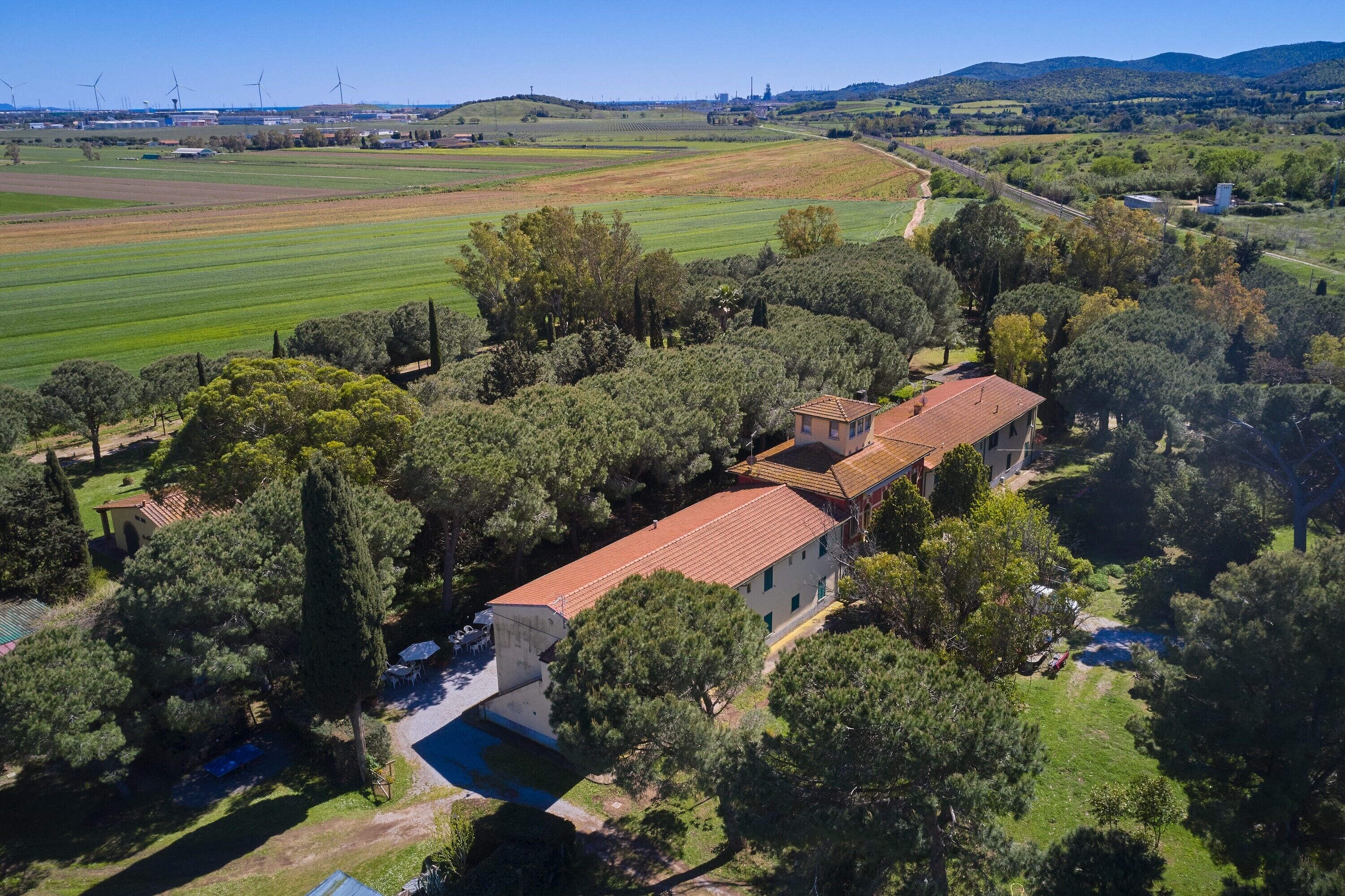 A large building with a red roof, surrounded by trees and fields.