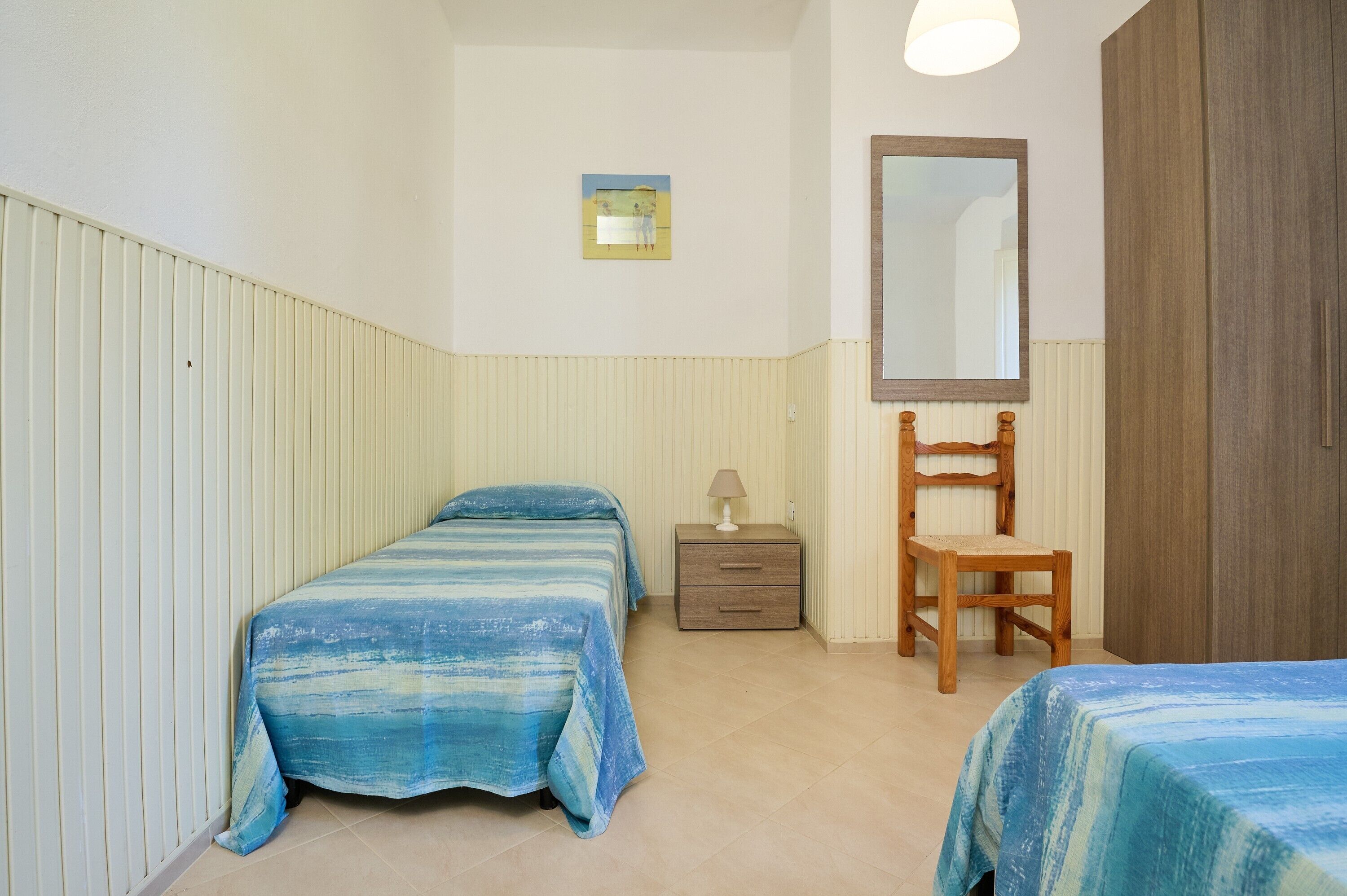 Un dormitorio con dos camas, una mesita de noche, una silla, un espejo y un cuadro en la pared.