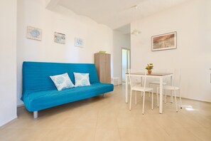 Une pièce avec un canapé bleu, des chaises blanches, une petite table sur laquelle se trouve un vase, et un meuble.