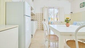 Uma cozinha com eletrodomésticos brancos, uma mesa de jantar com cadeiras e uma janela com cortina.
