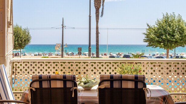 A balcony with two chairs and a table, overlooking a beach with palm trees and the sea. - Apartment '1a Linea San Juan Alicante' with Sea View, Wi-Fi and Air Conditioning (campello)