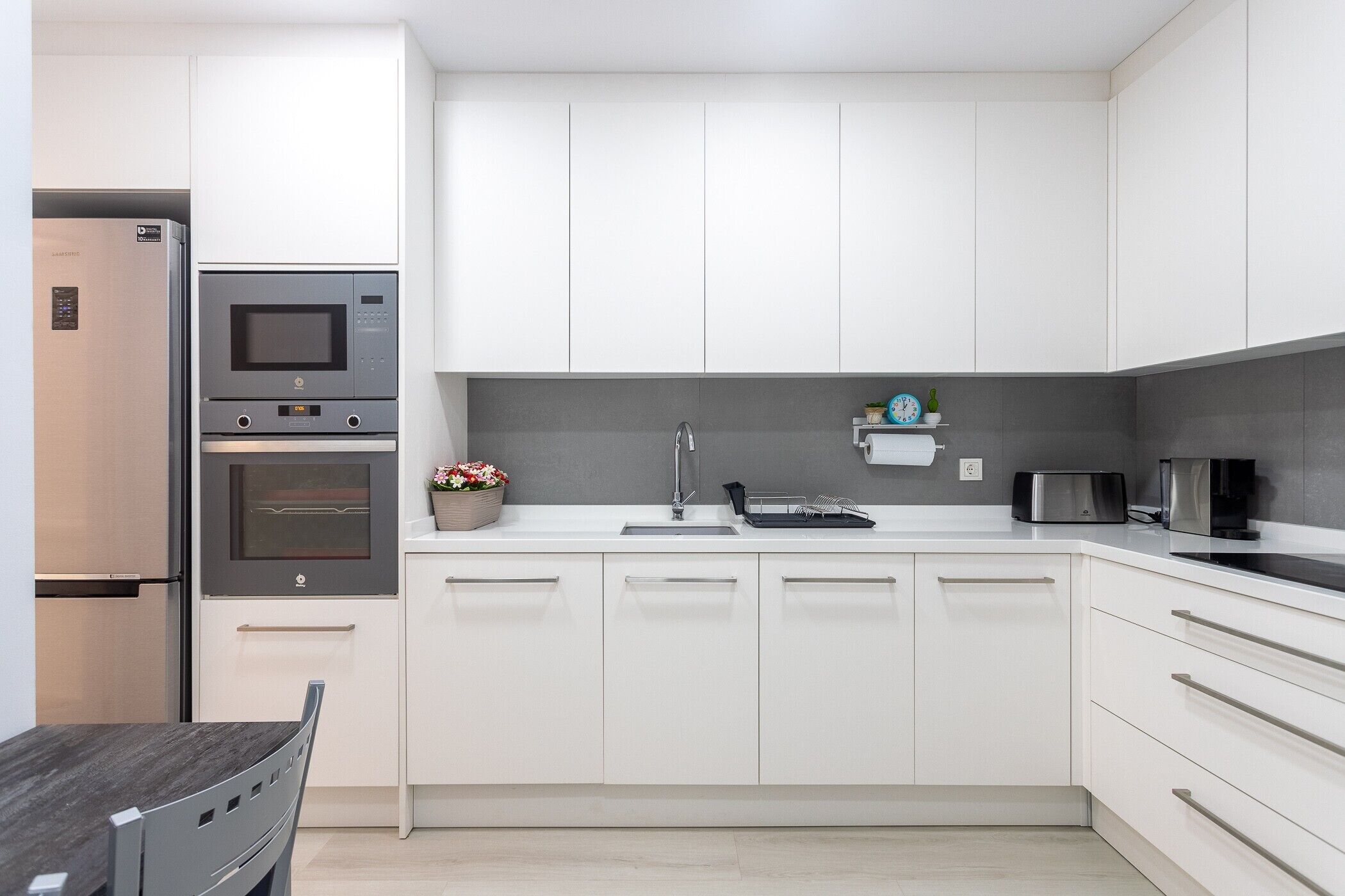 Una cocina moderna con gabinetes blancos, horno empotrado, microondas y tostadora.