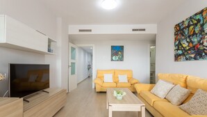 A modern living room with a TV, sofa, coffee table, and artwork. - Apartment '1a Linea San Juan Alicante' with Sea View, Wi-Fi and Air Conditioning (campello)