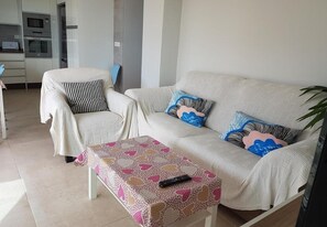 A living room with a sofa, a chair, a coffee table, and a kitchen in the background.