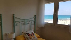 Ein Bett mit gelber Bettdecke und einem Kissen mit Schmetterlingsmuster, eine Nachttischlampe und ein Fenster mit Blick auf den Strand.