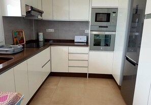 A kitchen with white cabinets, a microwave, an oven, a toaster, and a sink.
