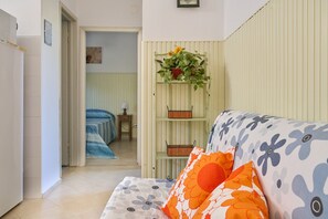 A room with a bed, a green shelf with baskets, a sofa with floral cushions, and a door leading to another room. - Apartment 'Mare Etrusco 3' with Shared Garden and Wi-Fi (Populonia)