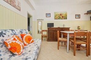 A living room with a sofa, a dining table with chairs, a TV, and a kitchen area. - Apartment 'Mare Etrusco 3' with Shared Garden and Wi-Fi (Populonia)