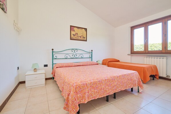 Una camera da letto con due letti, un comodino, una lampada, una finestra e un quadro appeso al muro.