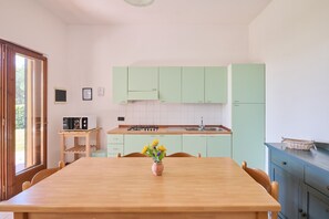 Una cucina con mobili verde chiaro, un tavolo di legno con sedie, un vaso di fiori e un forno a microonde su uno scaffale.
