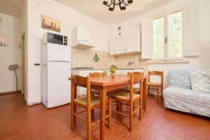 Une cuisine de taille réduite comprenant une table à manger, des chaises, un réfrigérateur et une fenêtre avec des rideaux.