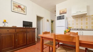 A kitchen with a wooden table, chairs, a TV, and a refrigerator. - Apartment 'Mare Etrusco 2' with Shared Garden and Wi-Fi (Populonia)