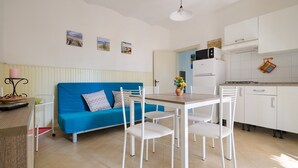 Ein kompakter Wohnbereich mit blauem Sofa, weißen Esstischen, einer Küchenzeile mit weißen Schränken und einem kleinen Esstisch.