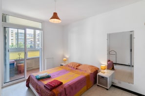 Une chambre à coucher comprenant un lit, des lampes de chevet, un miroir et une porte-fenêtre coulissante donnant sur un balcon.