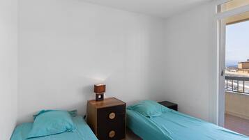 Ett litet, rent rum med två enkelsängar, ett träbord vid sängen med en lampa och en balkong med utsikt.