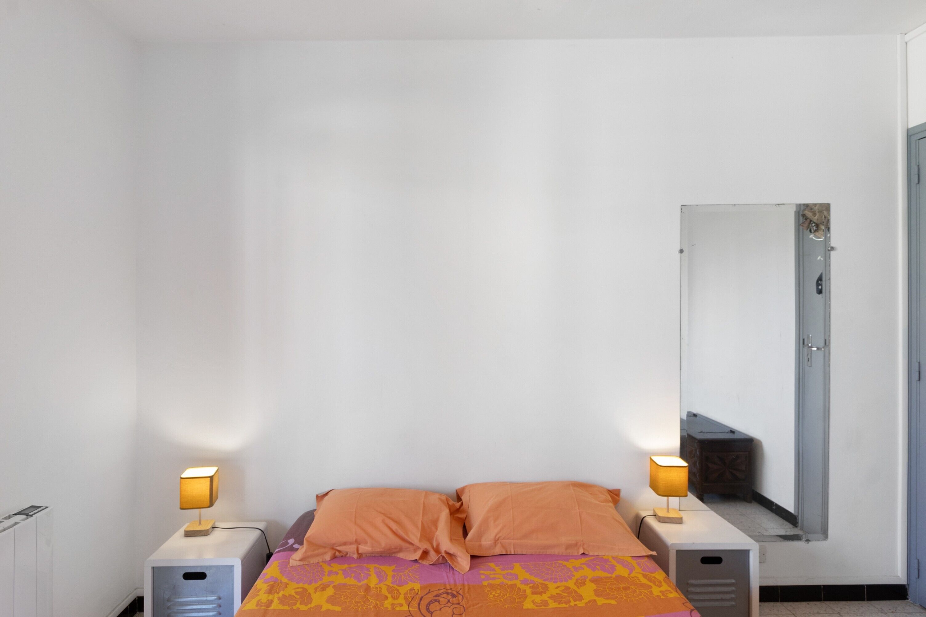 Une chambre à coucher avec un lit, deux lampes de chevet, un miroir et un radiateur.