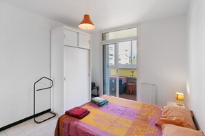 Une chambre à coucher comprenant un lit, une armoire, un radiateur, une fenêtre et un balcon.