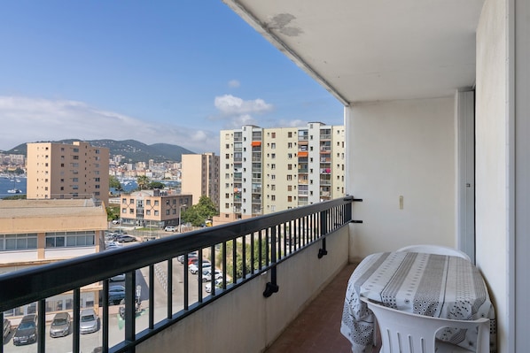 Un balcon offrant une vue sur le paysage urbain, avec des immeubles de grande hauteur et une étendue d’eau.