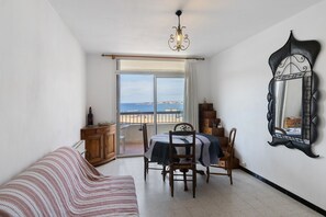 Ett rum med ett matbord, stolar, en soffa, en spegel och utsikt över havet genom ett stort fönster.
