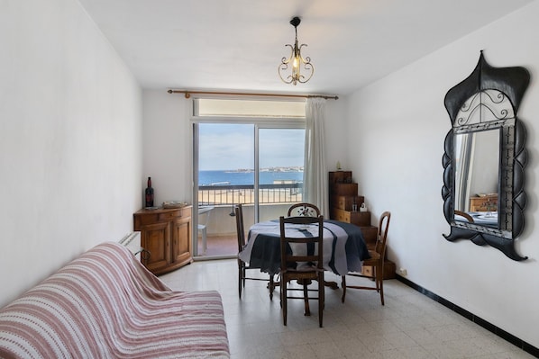 Une pièce comprenant une table à manger, des chaises, un canapé, un miroir et une vue sur la mer, visible à travers une grande fenêtre.