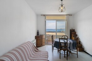 Une pièce comprenant un canapé, une table à manger avec des chaises, un buffet en bois et une vue sur la mer, visible à travers une porte vitrée.