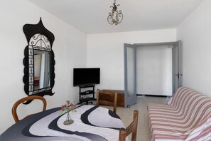 Ein Zimmer mit Esstisch, Stühlen, Fernseher, einer Couch, einem Spiegel und einer Tür zu einem anderen Raum.