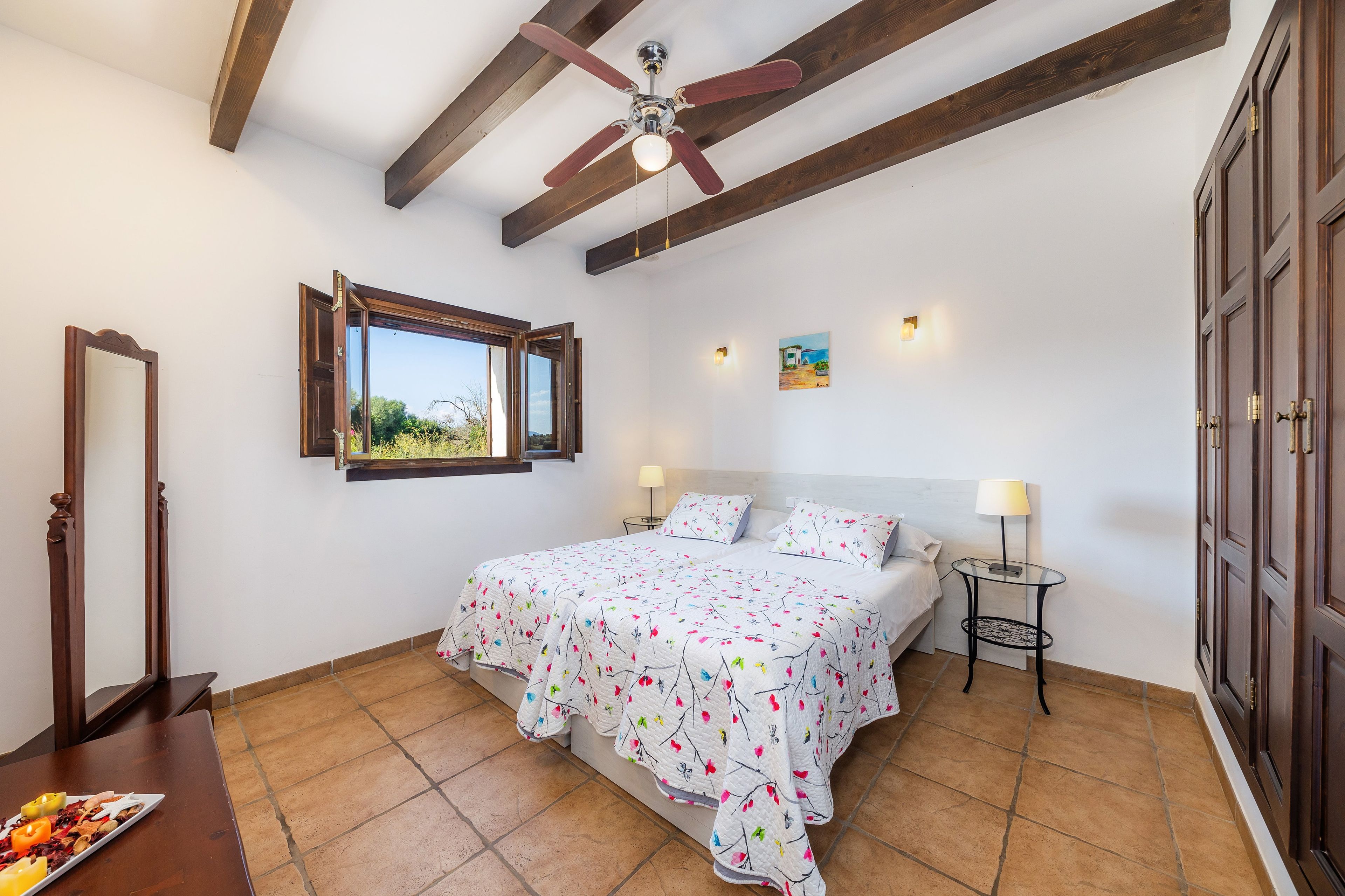 A bedroom with a bed, a window, a ceiling fan, a bedside table, and a lamp.