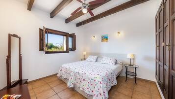 A bedroom with a bed, a window, a ceiling fan, a bedside table, and a lamp.