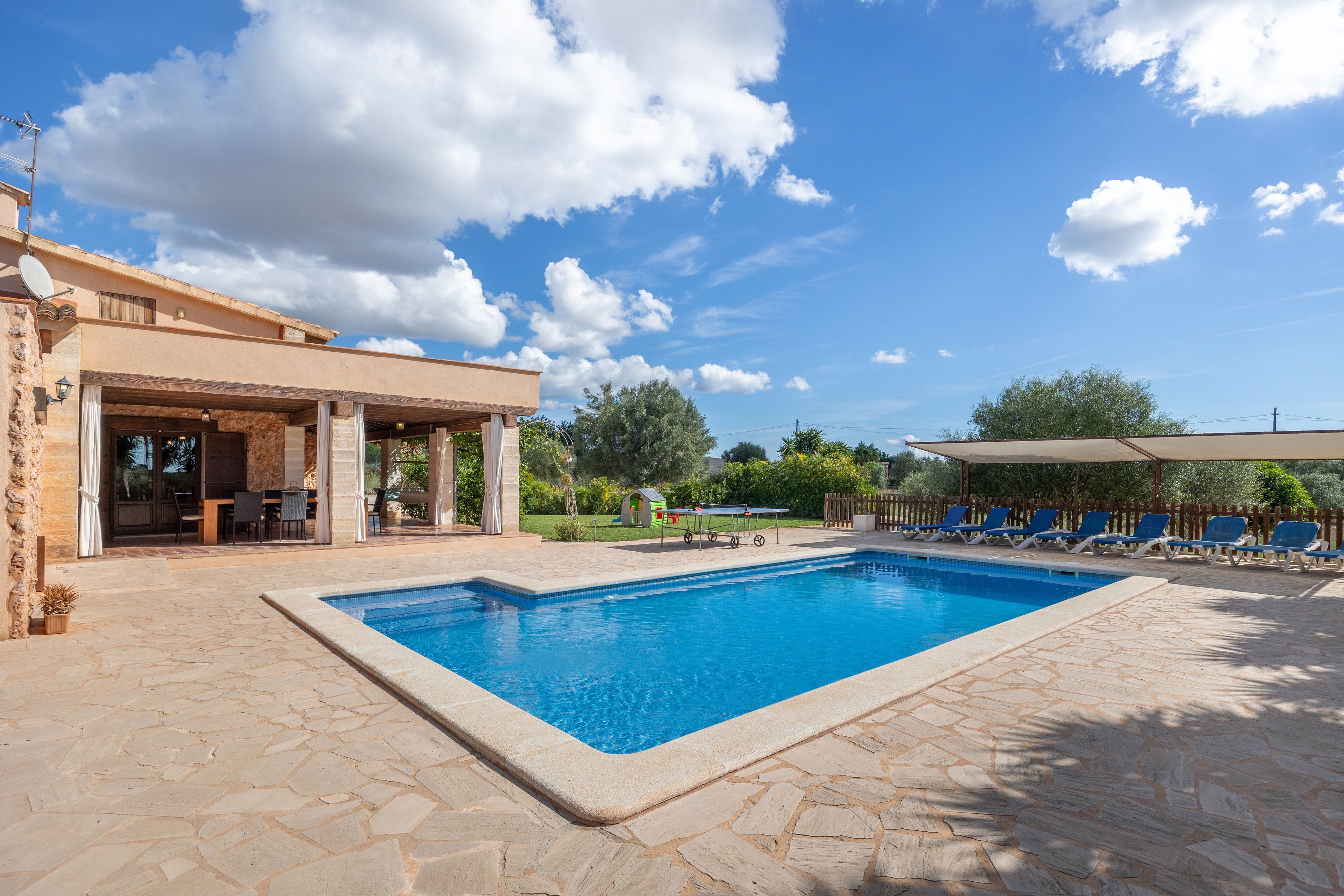 A swimming pool with a stone deck, a covered patio with outdoor furniture, and a view of the sky.