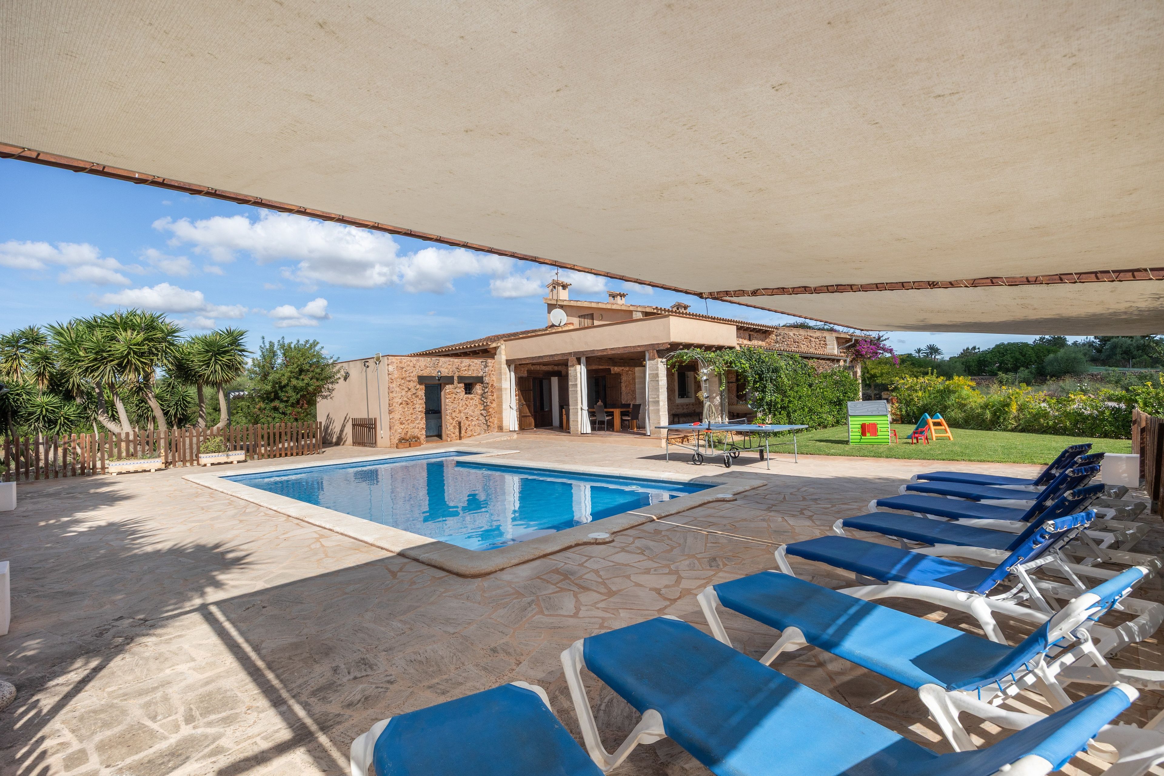 A pool area with lounge chairs, a covered patio, and a stone building with a tower.