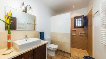 A bathroom with a sink, mirror, toilet, shower, and a towel rack.