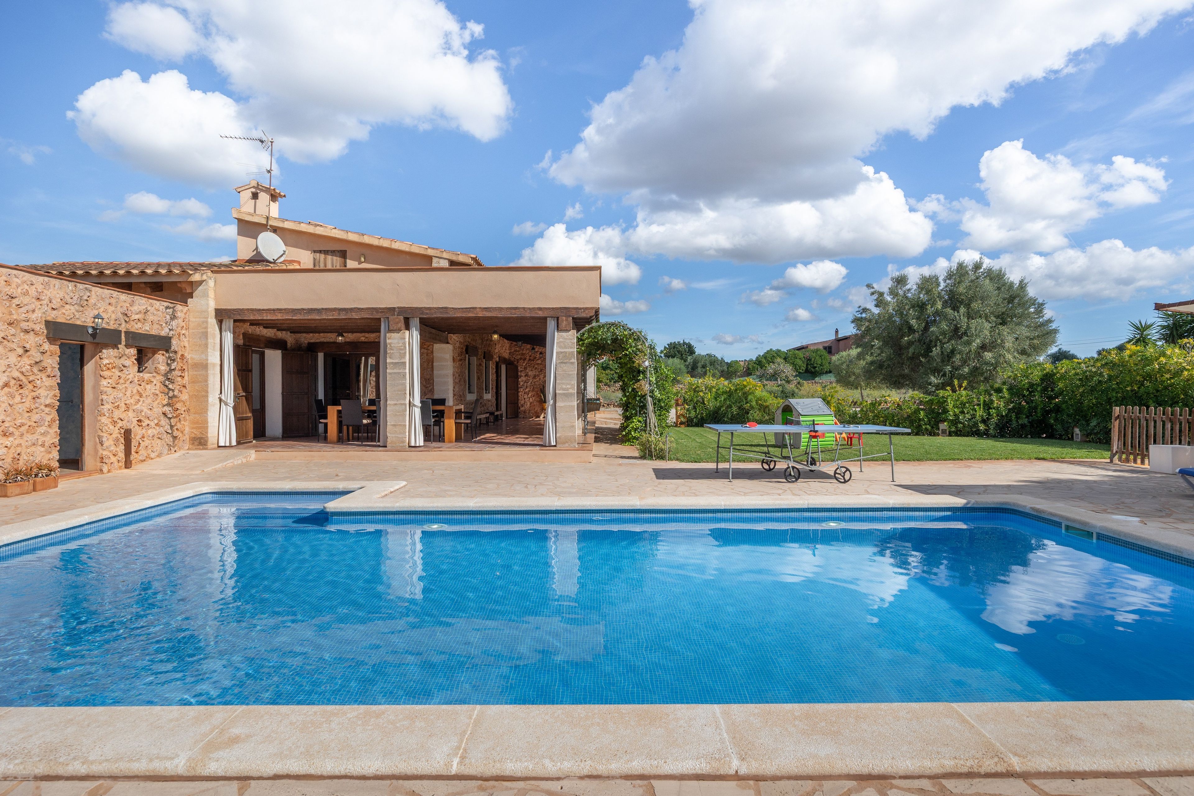 Una piscina con zona de patio, un espacio de estar techado al aire libre y vista a un edificio residencial al fondo.