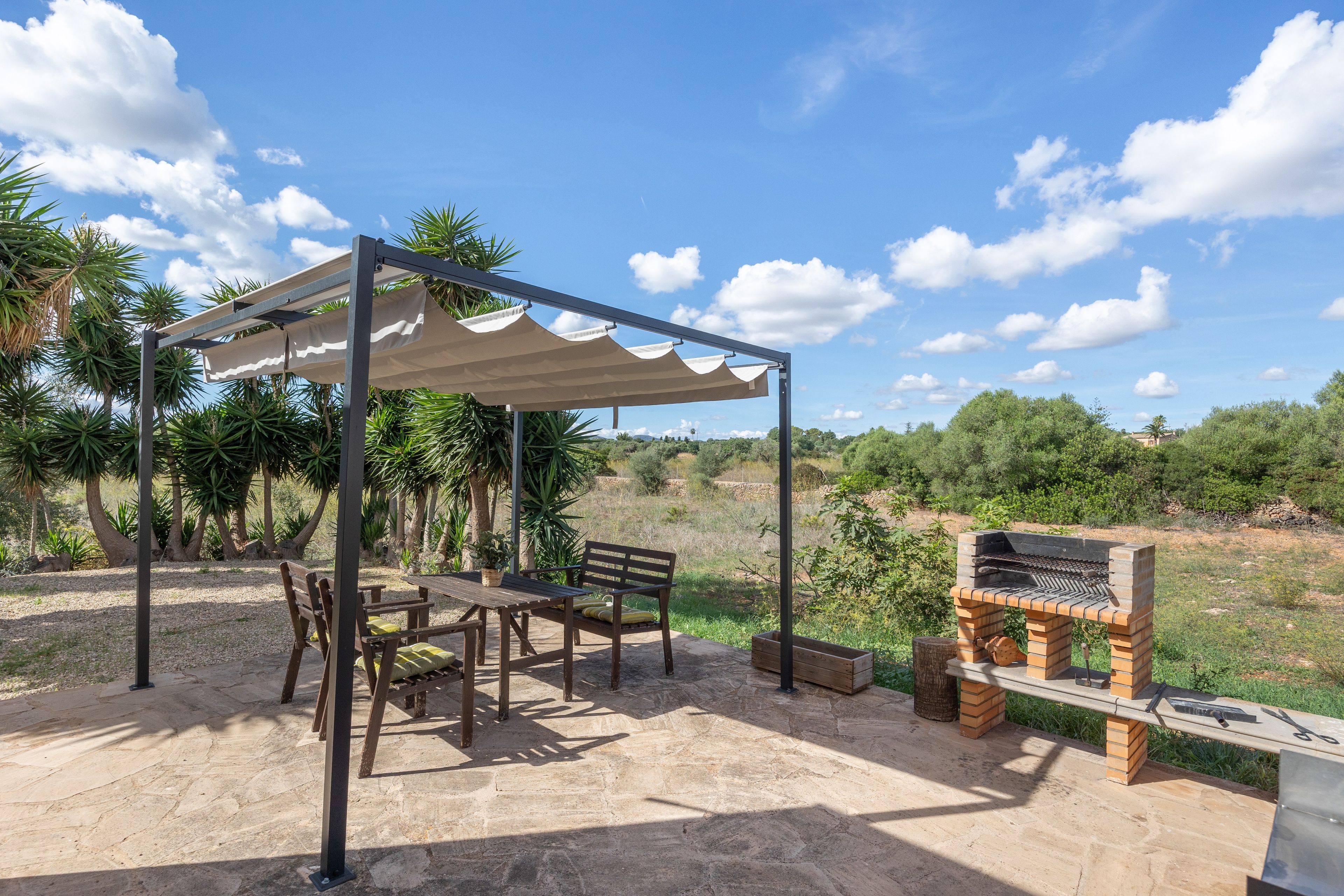An outdoor patio with a pergola, a wooden table, chairs, and a barbecue grill.