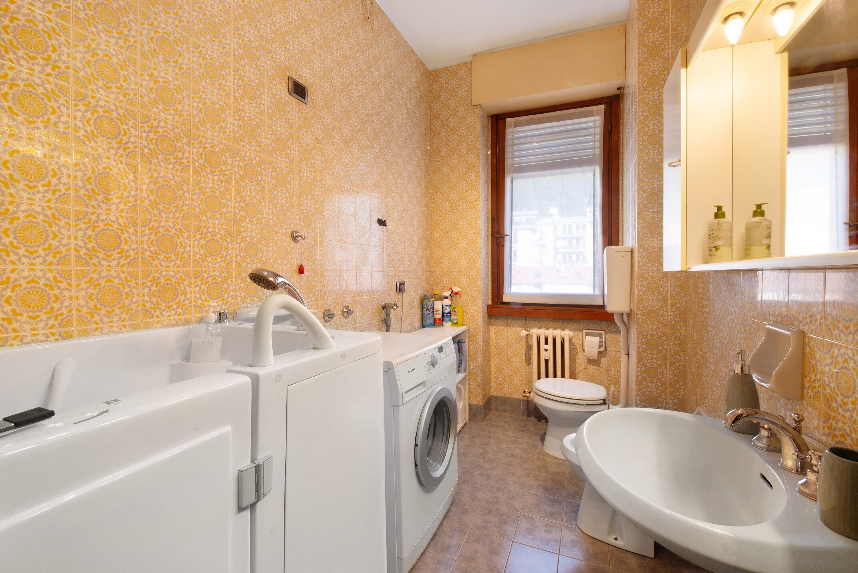Une salle de bain équipée d’un lave-linge, d’une baignoire, de toilettes et d’un lavabo.
