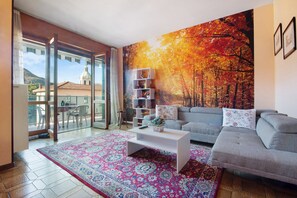 A living room with a sofa, a coffee table, a bookshelf, and a large autumn-themed wall mural. - Holiday Home "House of Roses" with Private Terrace and Wi-Fi (Como)