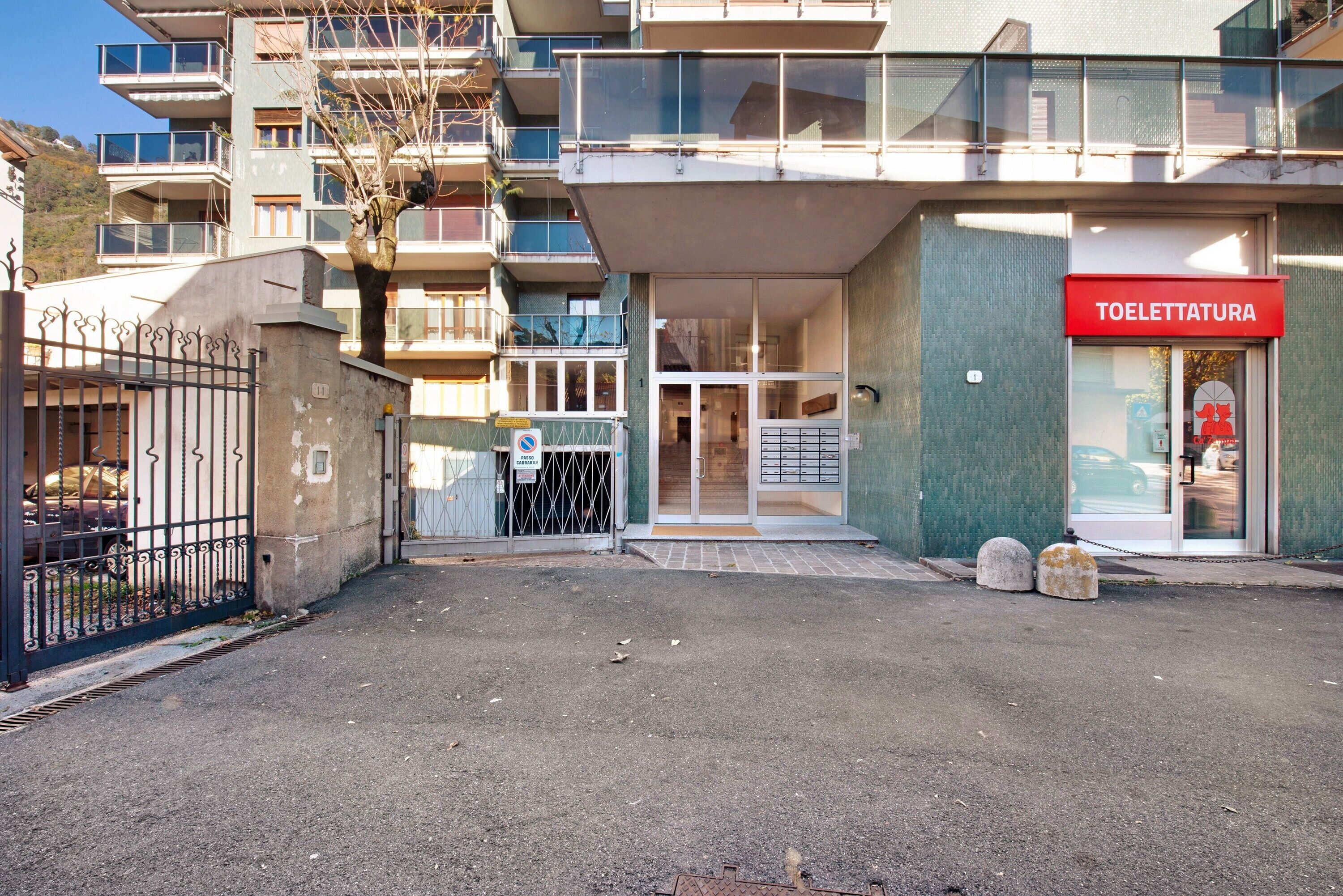 A multi-story building with a visible entrance, a sign reading 'TOLETTATURA,' and a gated driveway.