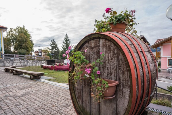 A wooden barrel with flower pots on top, located in an outdoor setting with a paved area and benches.
