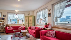 Una sala de estar con sofás rojos, una mesa de centro de madera y vistas a montañas a través de las ventanas.