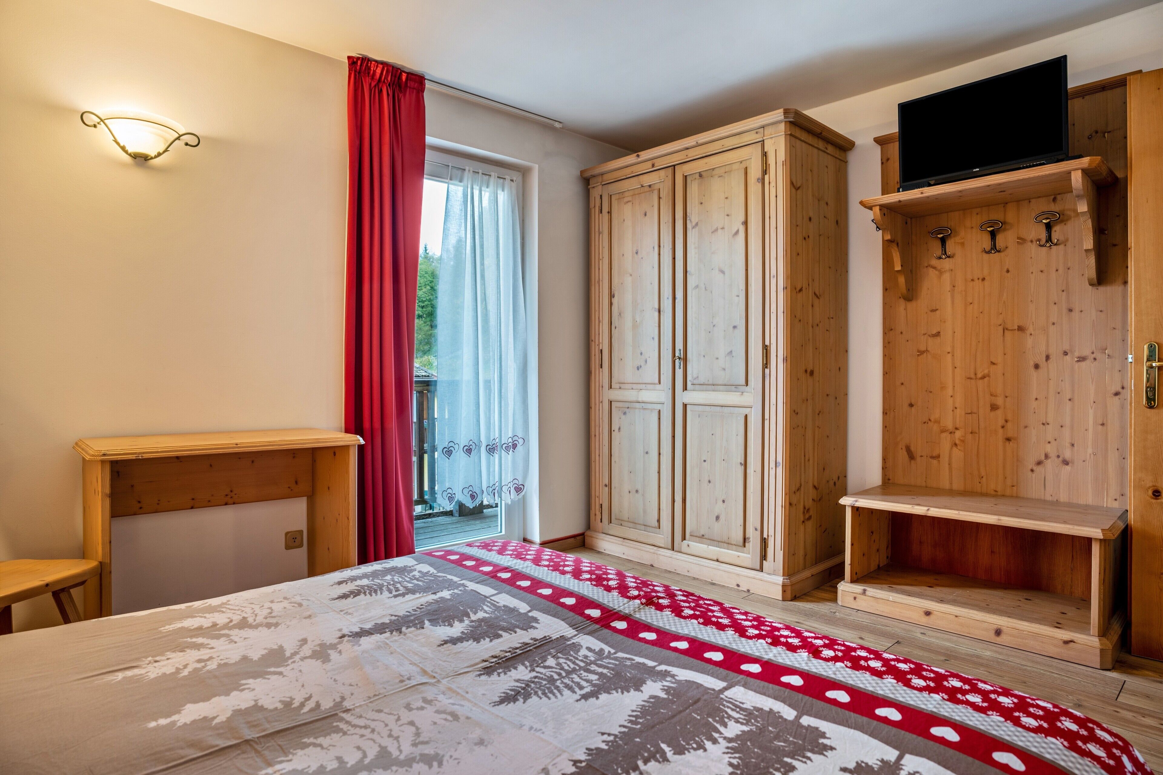 A bedroom with a bed, wooden wardrobe, and a television on a shelf.