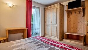 Un dormitorio con cama, armario de madera y televisor sobre una estantería.
