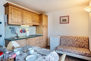 A kitchen with wooden cabinets, a tiled backsplash, a dining table set with plates and cups, and a sofa with a floral pattern.