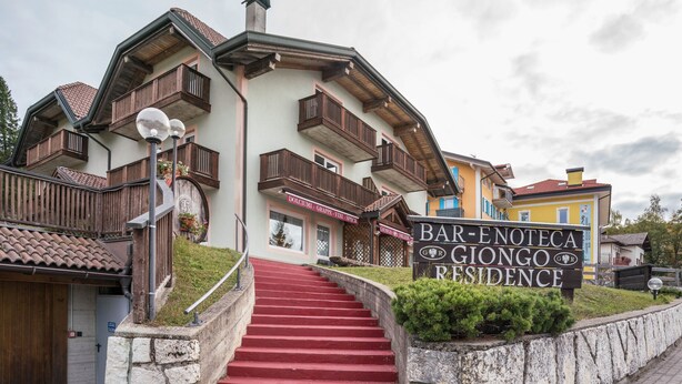 Un edificio de varios pisos con una escalera roja que conduce a una puerta identificada como 'Bar-Fnoteca Giongo Residence'.