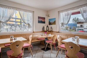 A cozy dining area with wooden benches and chairs, a table with a bottle of wine, and a scenic view through the windows.